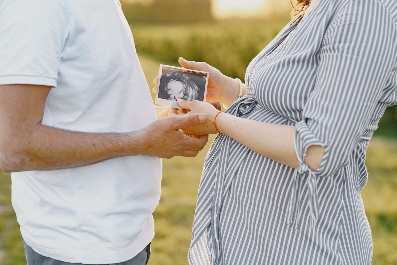 An expectant couple outdoors holding an ultrasound photo together