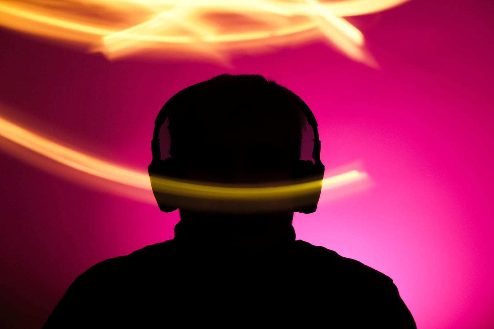 Silhouette of a person wearing headphones against pink light streaks