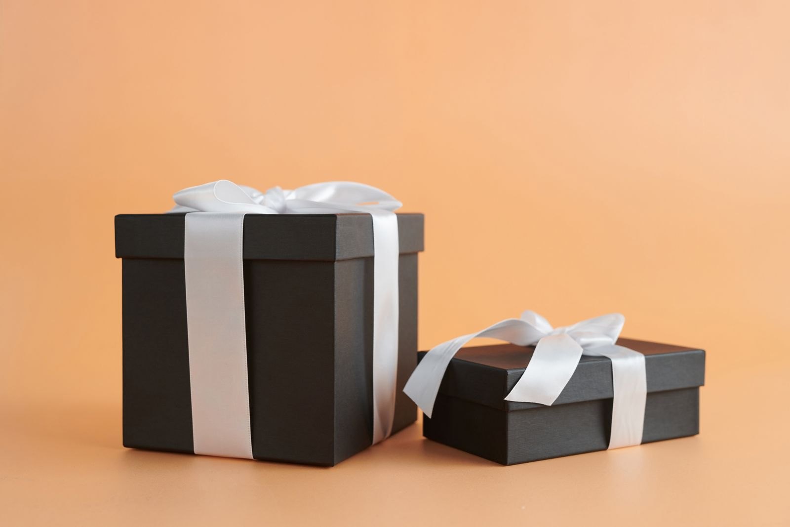 Two black gift boxes tied with white ribbons on a peach background