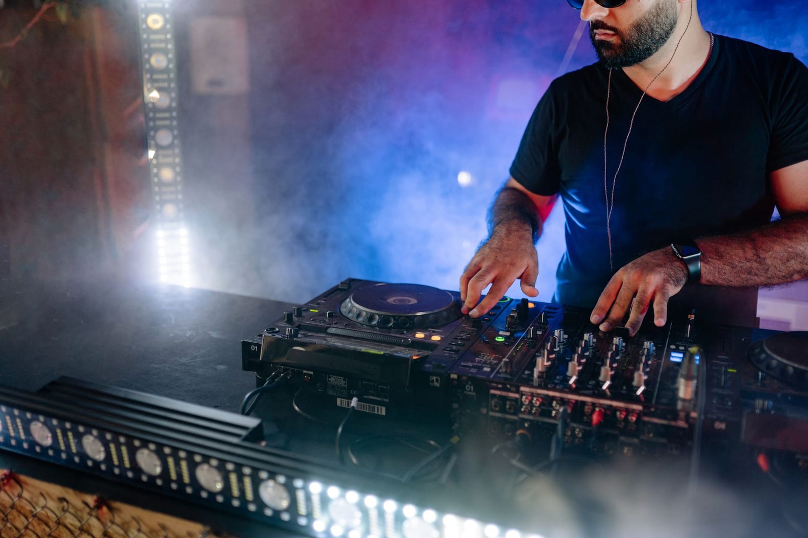A DJ performing live with mixing equipment in a colourful club