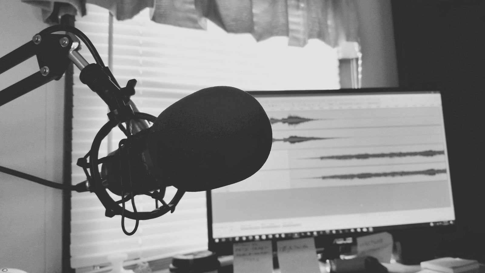 A black and white podcast setup with a microphone in front of a screen showing an audio waveform