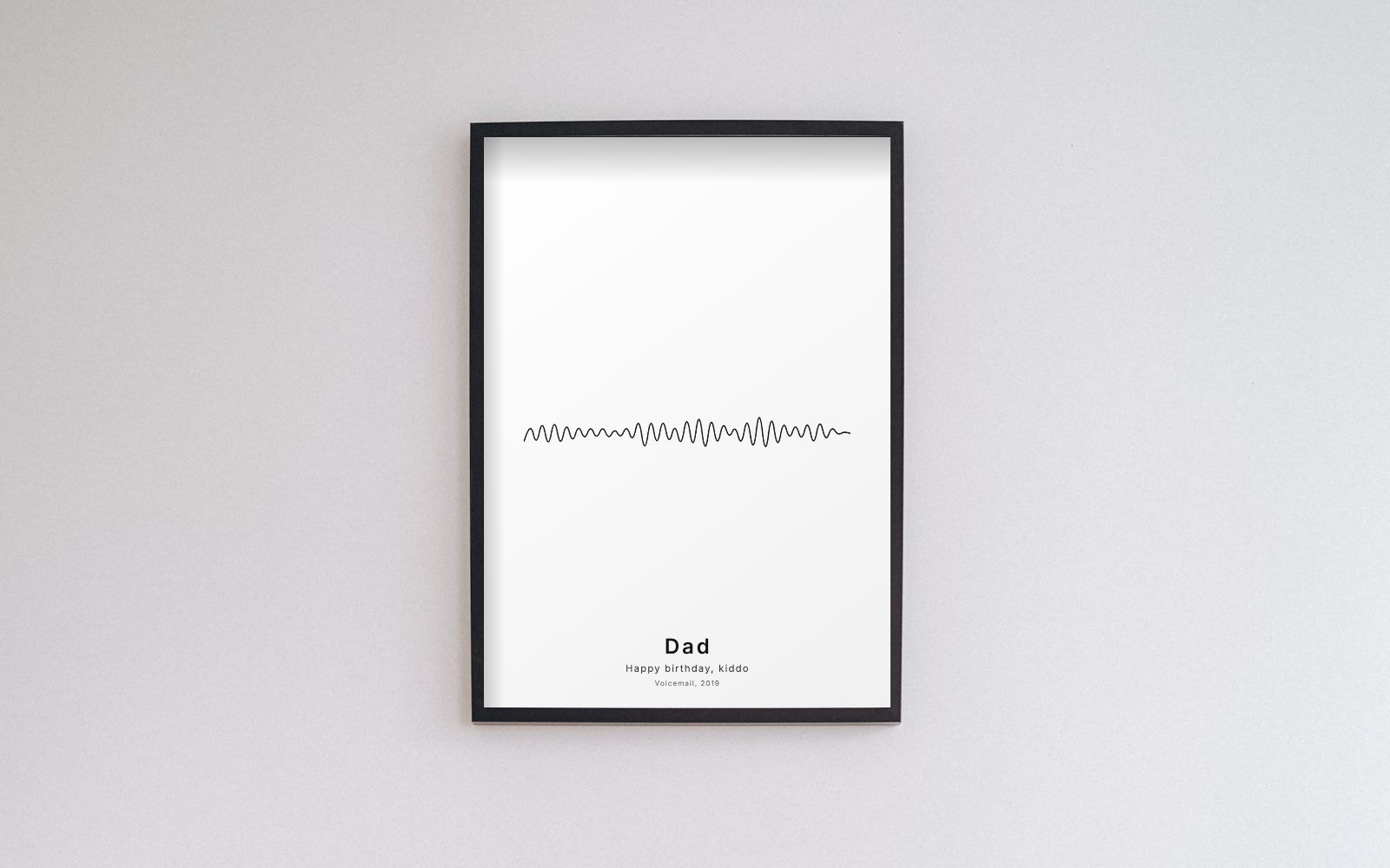 A black frame on a white wall holding a minimal sound wave print with a thin black voice waveform and the title Dad