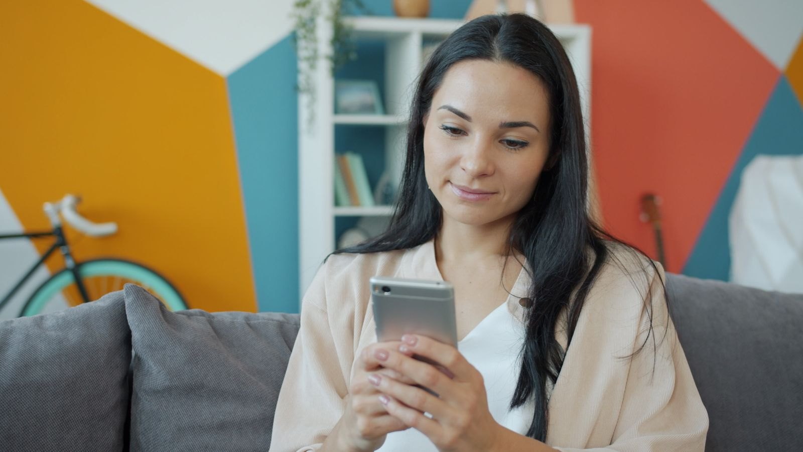 A woman relaxing on a sofa while using her smartphone in a colourful living room