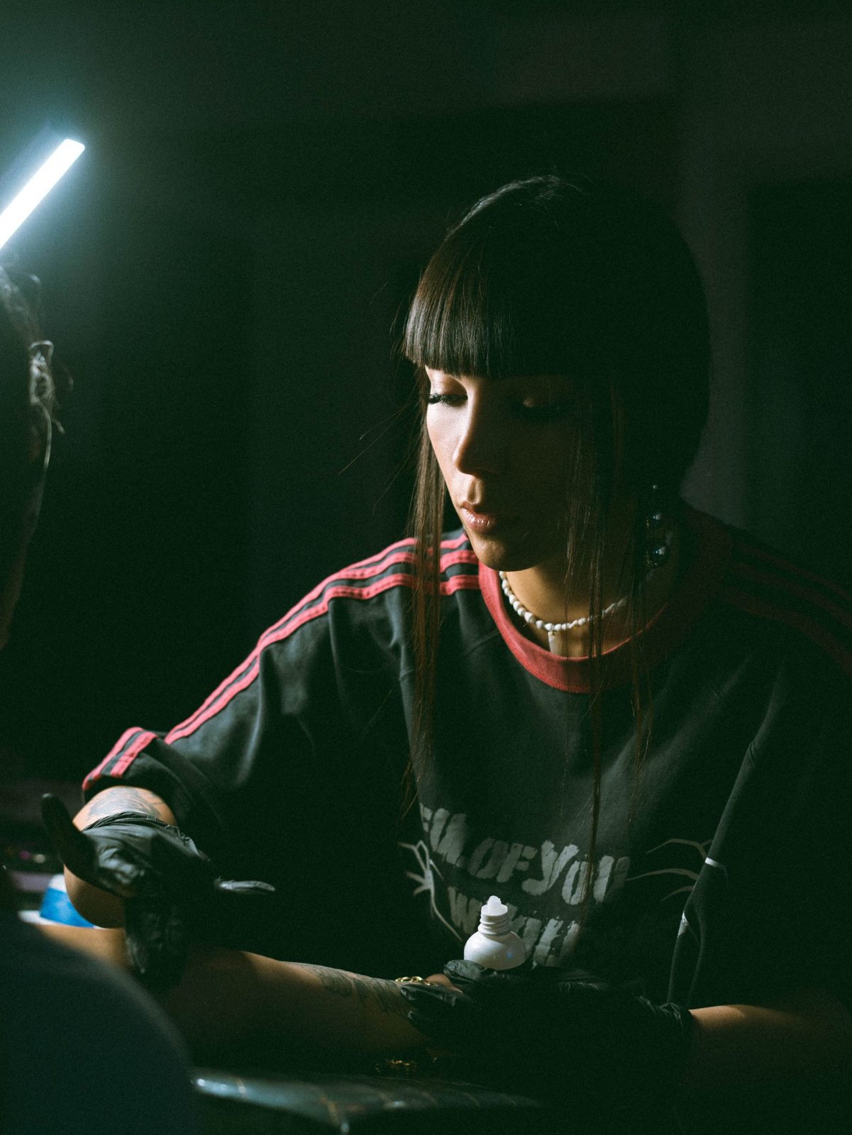 A tattoo artist in a dimly lit studio carefully working on a client's arm