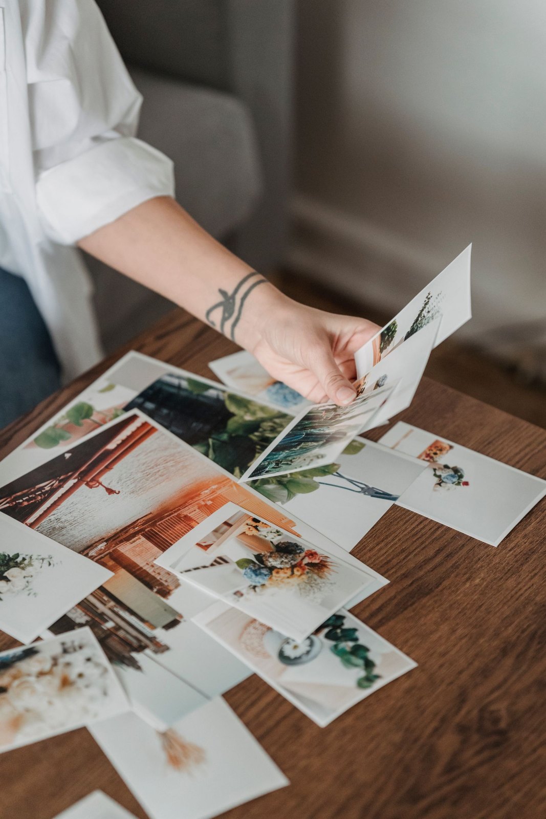A person looking through printed photographs spread across a wooden table