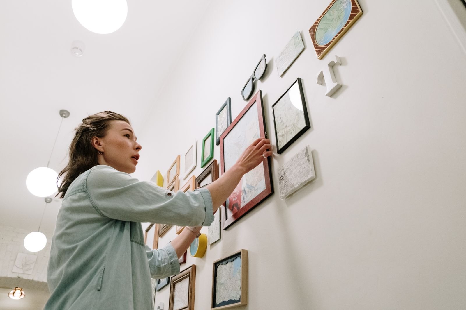 A woman arranging framed pictures on a bright white wall