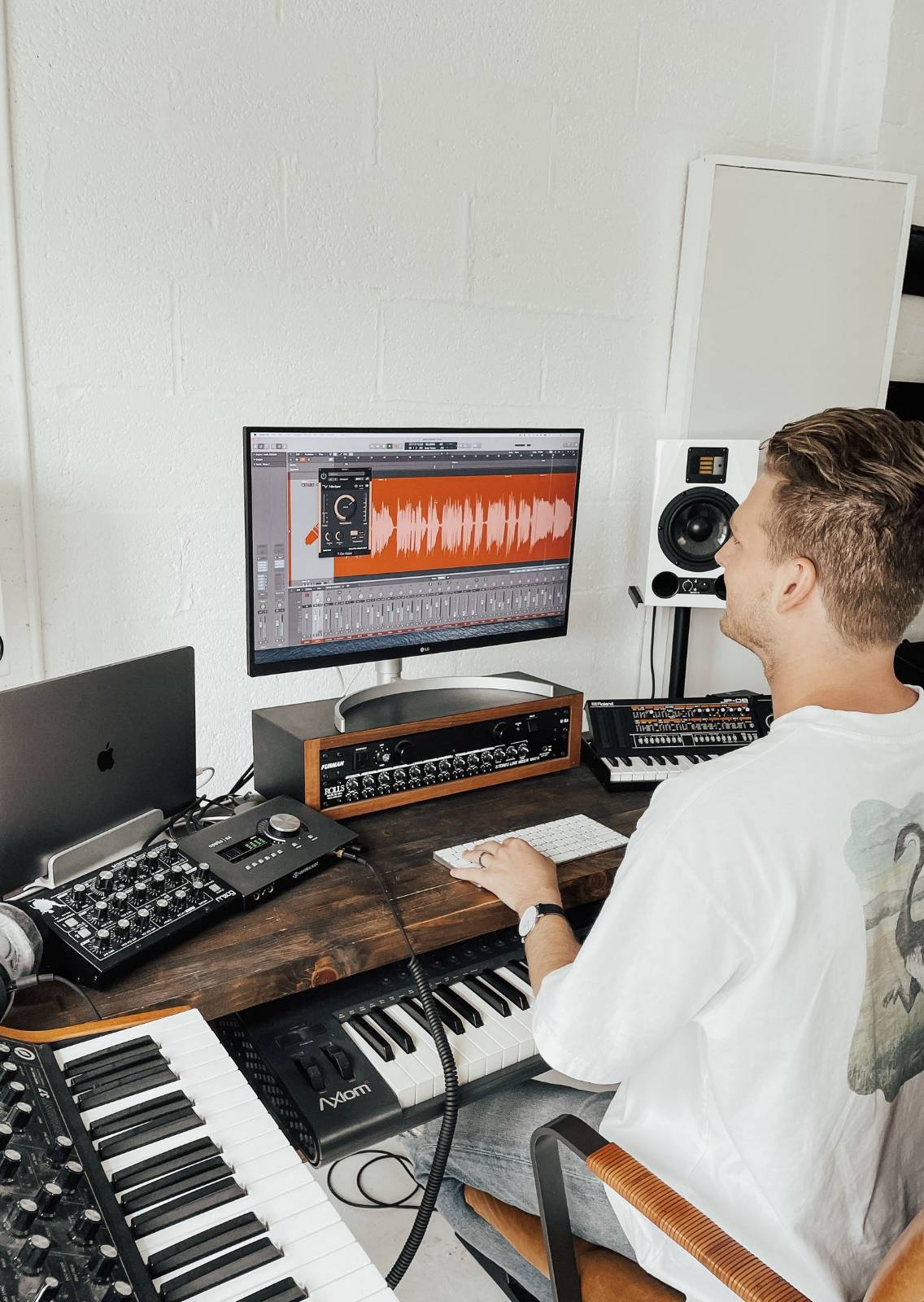 A music producer at a desk with a computer screen showing an orange audio waveform in editing software