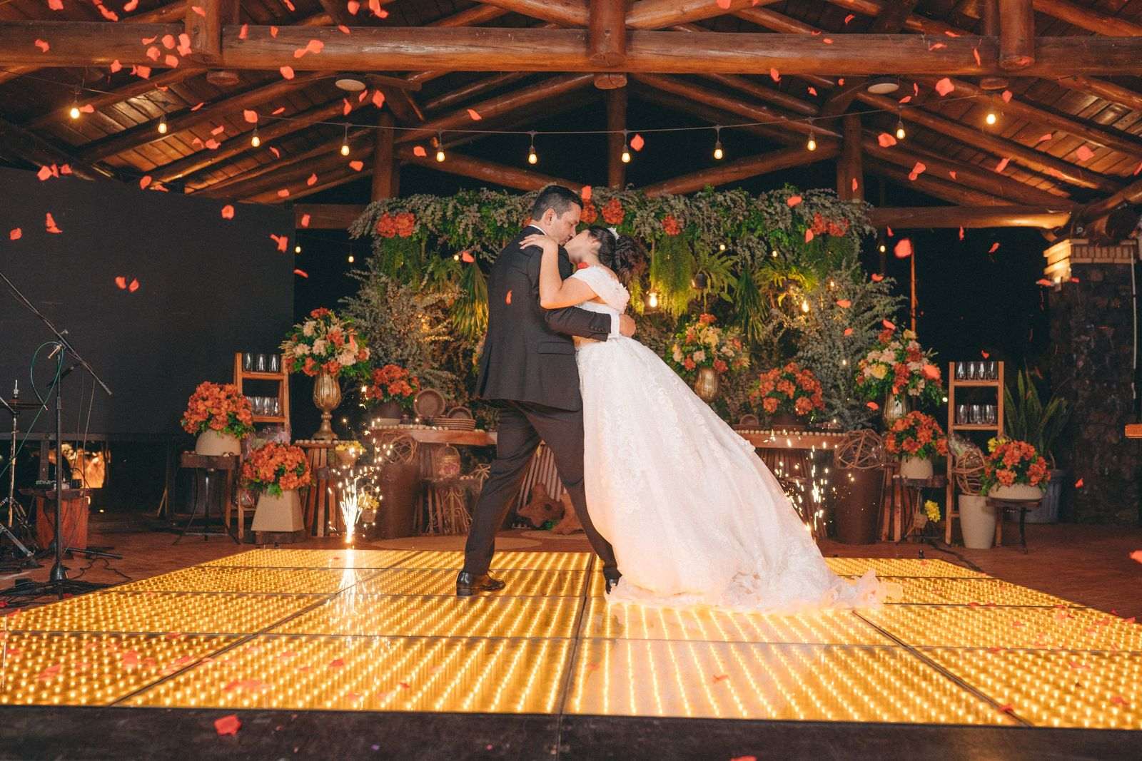 A bride and groom sharing their first dance on a lit, flower-decorated dance floor