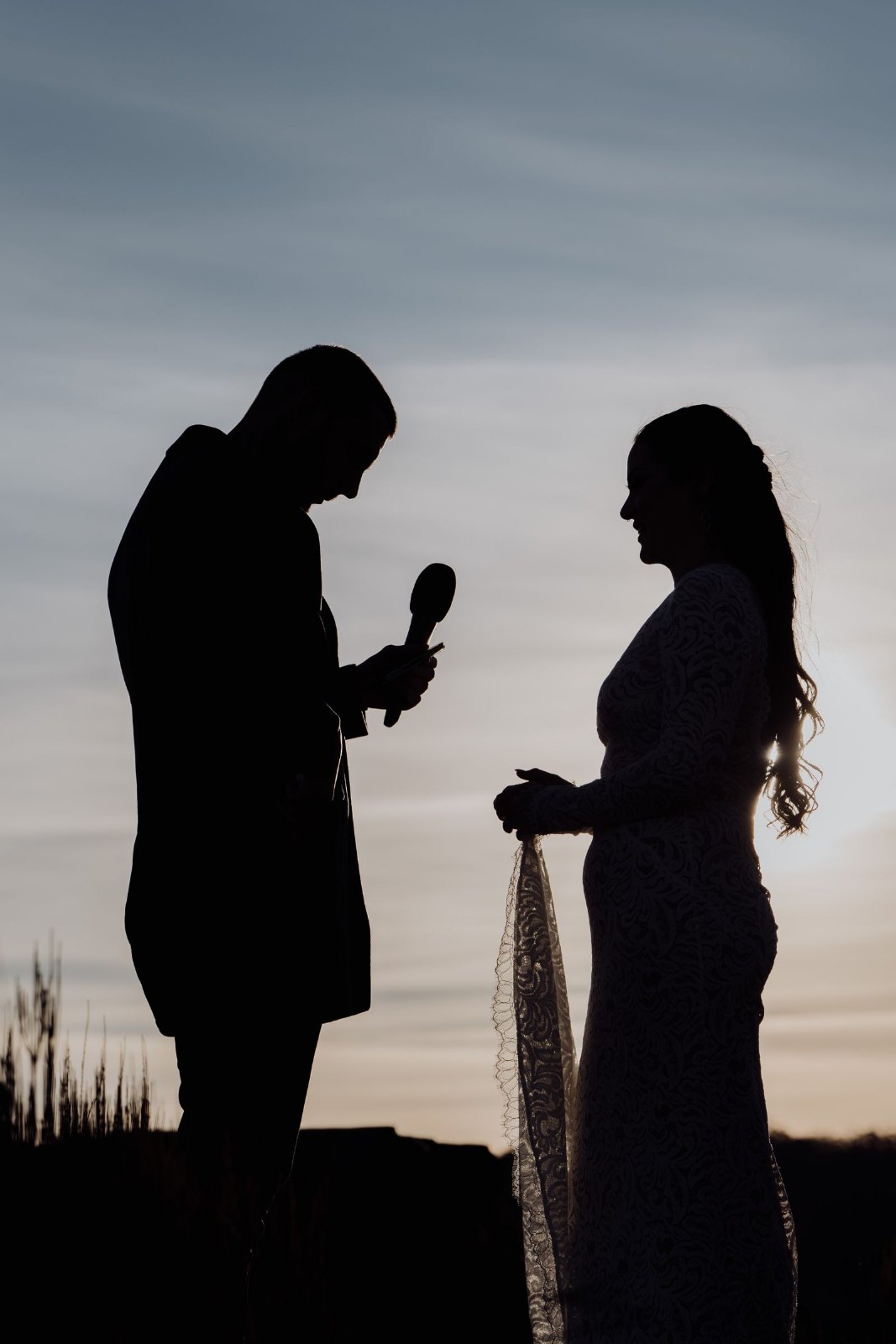 Silhouetted newlyweds exchanging vows against a sunset sky in the mountains